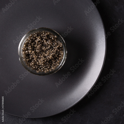 Sturgeon black caviar in glass can on black background. Top view.