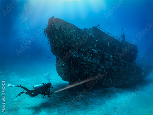 Fotografie, Obraz A scuba diver with a torch explores a sunken shipwreck at the seabed of the Mald