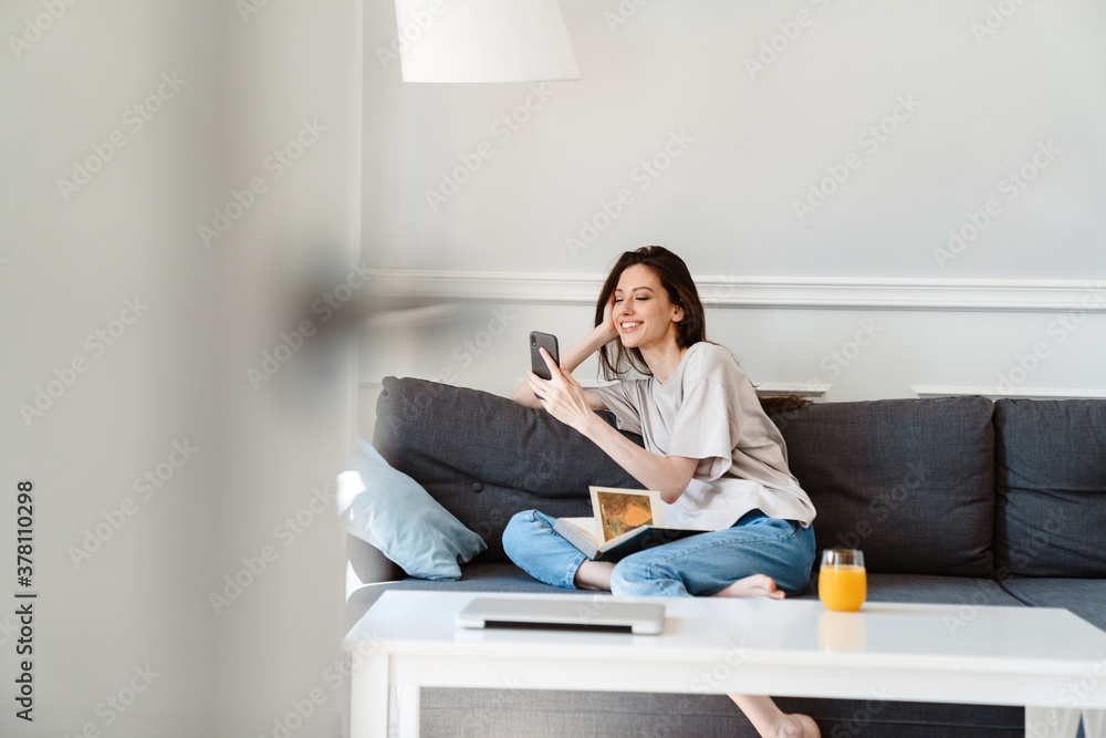 © Drobot Dean - Photo of joyful beautiful girl using cellphone while sitting on couch