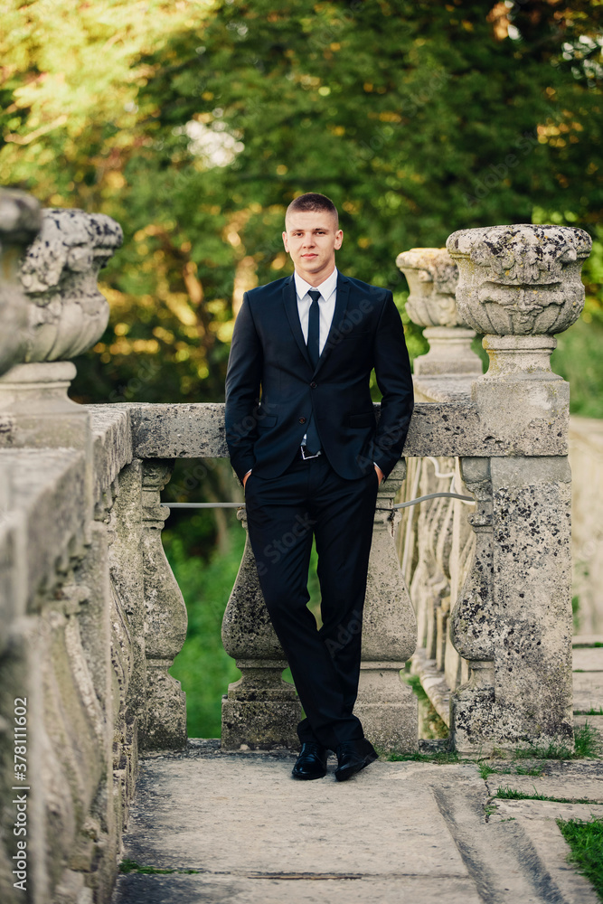 Fashionable model groom standing on the balcony leaning on railing Fashionable model groom standing on the balcony leaning on railing