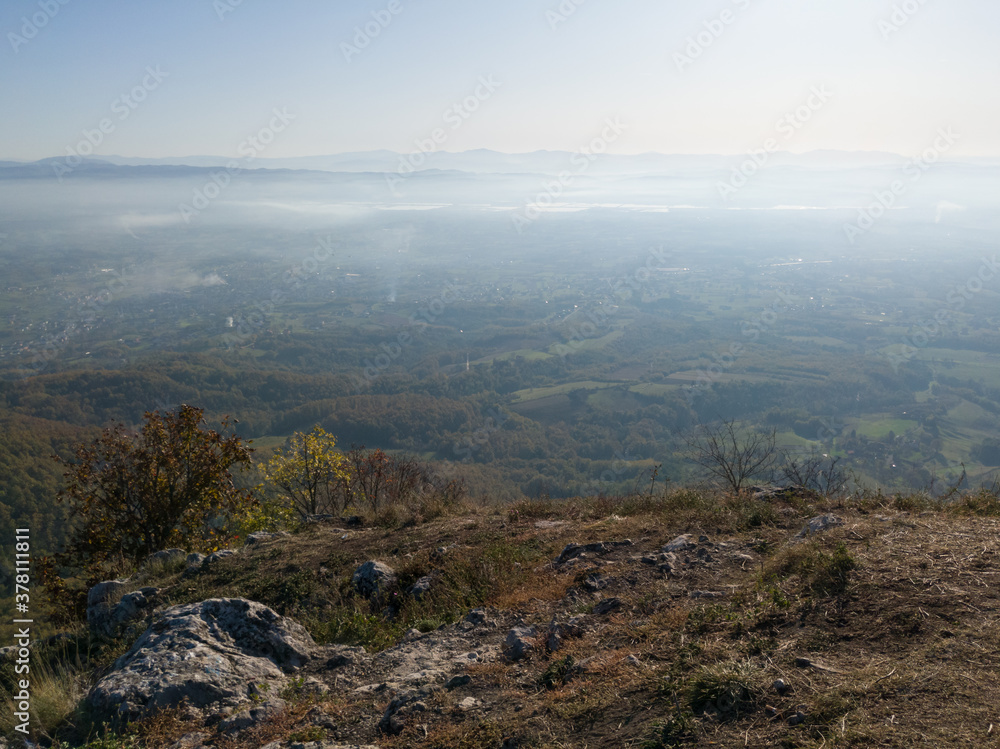 Scenic view from Kozara mountain to the valley filled with fog and smoke during a sunny day. Scenic view from Kozara mountain to the valley filled with fog and smoke during a sunny day.