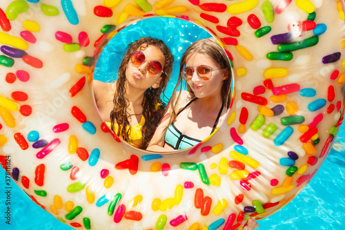 Two happy girls inside the inflatable buoy smile wearing near swimming pool in sunglasses with kiss gesture