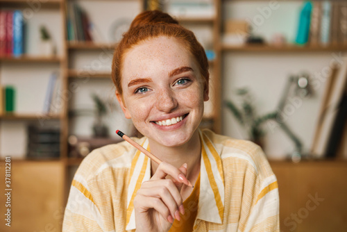 Image of happy redhead girl doing homework while sitting at table