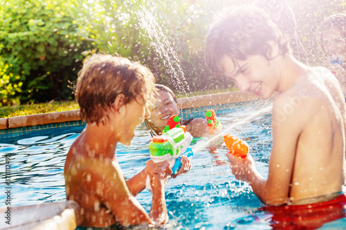 Canvas Print Happy laughing teenagers friends play with water-gun squirt pistol on swimming p