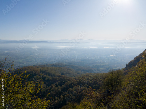 Scenic view from Kozara mountain to the valley filled with fog and smoke during a sunny day.