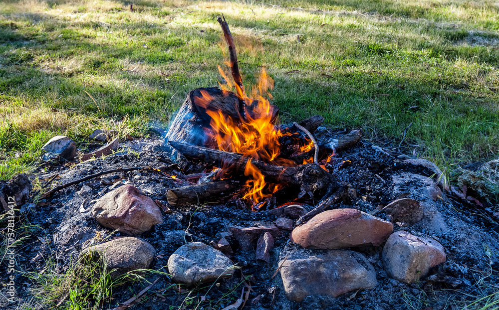 What remains of a camp fire left to burn overnight, the last of the logs burning with a small flame in the fire pit at a camp site. What remains of a camp fire left to burn overnight, the last of the logs burning with a small flame in the fire pit at a camp site.
