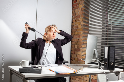 Totally depressed young employee at work with tangled telephone cable around her neck