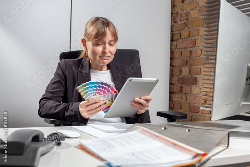 Young woman at work with a colorful palette in one hand and a tablet in the other, crying because she is overwhelmed with the task of choosing the right color photo