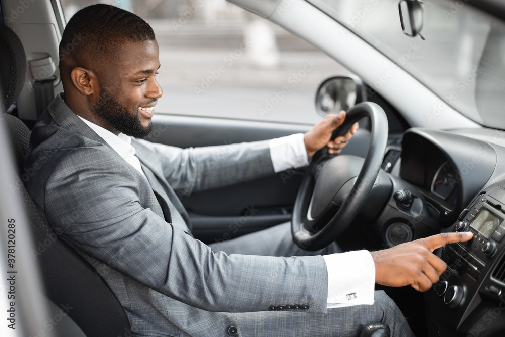 Smiling black businessman turning on music in his car Smiling black businessman turning on music in his car