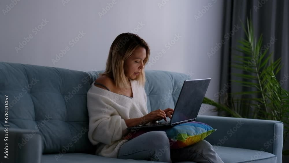 woman sits on the sofa in the living room and works at the laptop. evening twilight woman sits on the sofa in the living room and works at the laptop. evening twilight