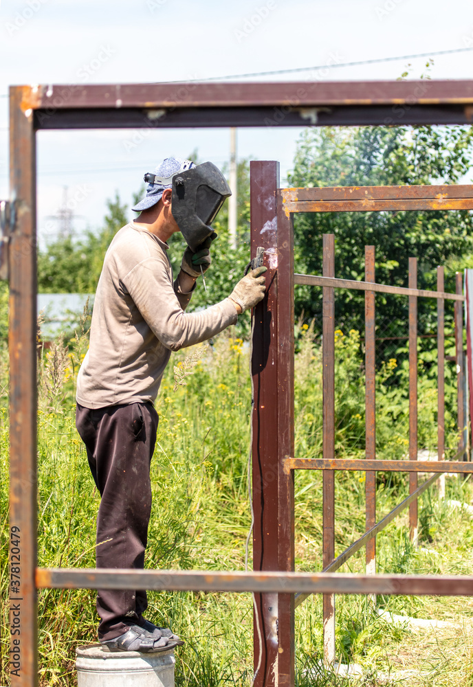 A worker welds metal for a fence. A worker welds metal for a fence.