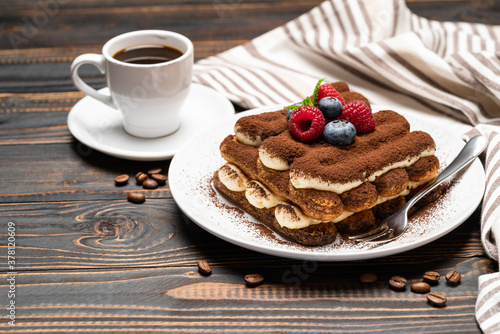 portion of Classic tiramisu dessert with raspberries, blueberries and cup of espresso coffee isolated on wooden background
