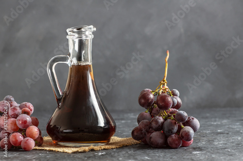 Glass bottle of organic black grape balsamic vinegar made from fermented fresh grapes. Healthy organic food black fruit, selective focus photo