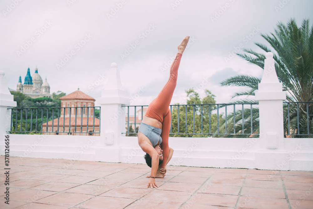 Sporty lady performing Urdhva Prasarita Eka Padasana position on terrace