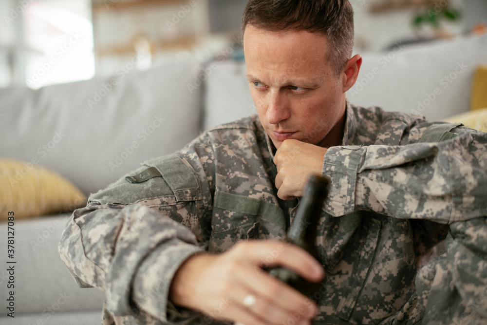 Depressed soldier with bottle sitting in livig room., Alcohol addiction...