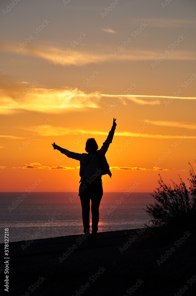 Silhouette of one girl at sunset, who stands on a mountain overlooking the sea. Vacation and tourism concept.