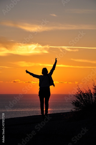 Silhouette of one girl at sunset, who stands on a mountain overlooking the sea. Vacation and tourism concept.