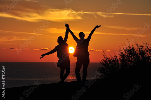 Silhouettes of two girls at sunset who stand on a mountain overlooking the sea. Vacation  concept.