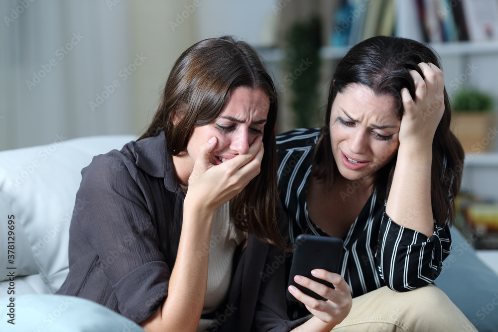 Sad friends or sisters crying checking smart phone Sad friends or sisters crying checking smart phone