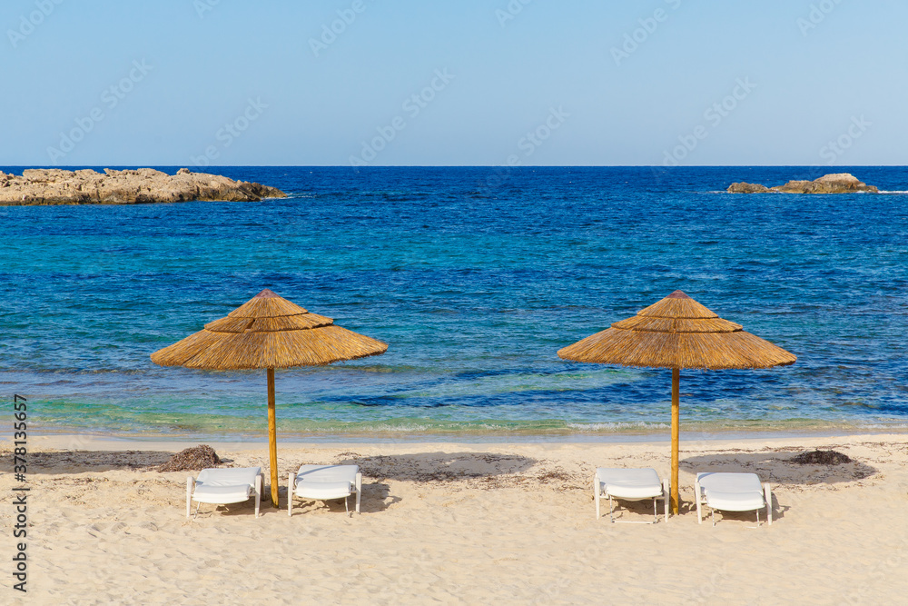 Sun beds and umbrellas on the sea coast of Formentera, Spain, the Mediterranean sea.