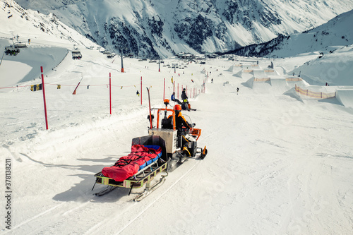 Snowmobile machine with sled and equipment riding fast hurry up driver to help injured skier or snowboarder at accident on winter mountain resort. Emergency rescue vehicle at ski slope piste downhil