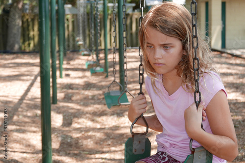 Sad girl sitting alone on a swing in a playground