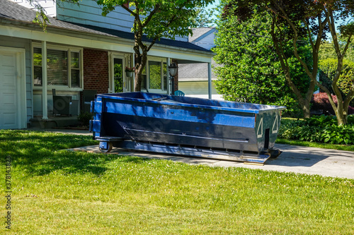 Photos A blue dumpster in the driveway of a house in a residential neighborhood