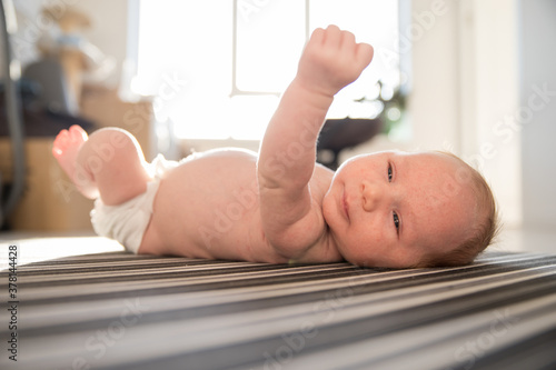 A newborn cute baby in a diaper restlessly lying on his back on striped sheets in day light photo