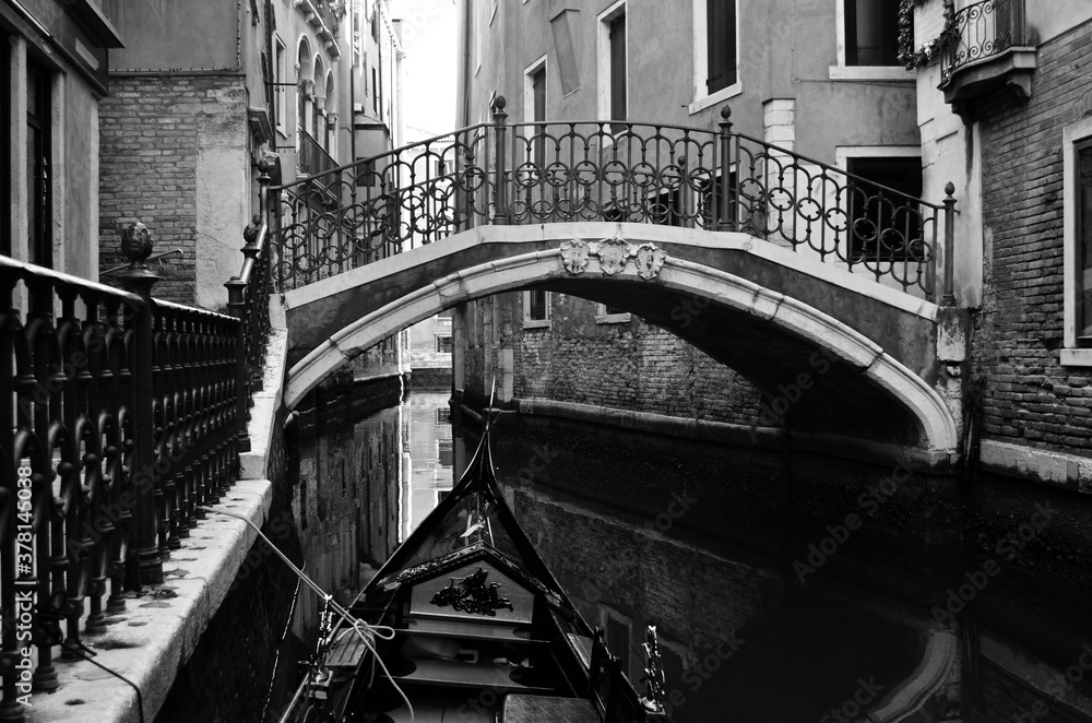 Fototapeta premium Venetian foreshortening in black and white with a typical bridge crossing a canal seen from a gondola