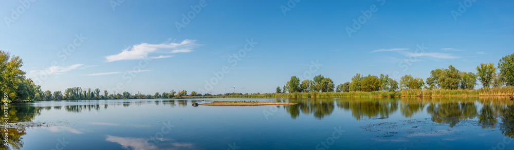 Panoramic view over a lake near Elbe river with wind turbines at sunny day and blue sky, Magdeburg, Germany..