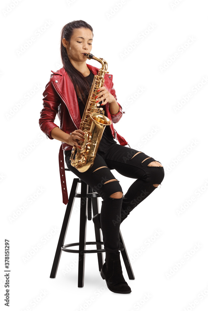 Fototapeta premium Female saxophonist in a red leather jacket playing sax while sitting on a chair