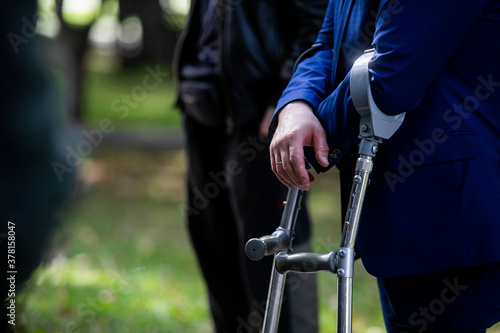 A disabled person with one leg in a strict suit walks on crutches.