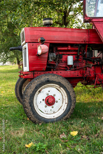 Old small red agriculture tractor parked on the grass summertime before sunset three-quarter view photo