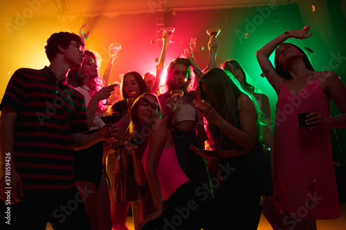 Cocktail. A crowd of people in silhouette raises their hands, dancing on dancefloor on neon light background. Night life, club, music, dance, motion, youth. Bright colors and moving girls and boys.