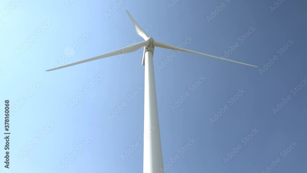 White windmill in the center, with blades turning, and with blue background in the sky White windmill in the center, with blades turning, and with blue background in the sky