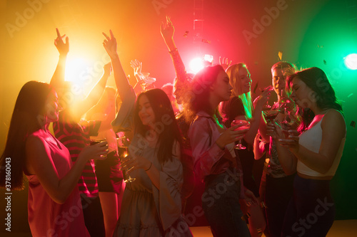 Motion. A crowd of people in silhouette raises their hands, dancing on dancefloor on neon light background. Night life, club, music, dance, motion, youth. Bright colors and moving girls and boys.