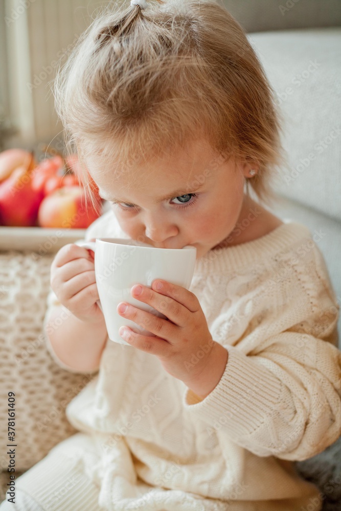 A little cute girl in an orange sweater is drinking tea. Cozy portrait of a girlsitting at home. Fall. A little cute girl in an orange sweater is drinking tea. Cozy portrait of a girlsitting at home. Fall.