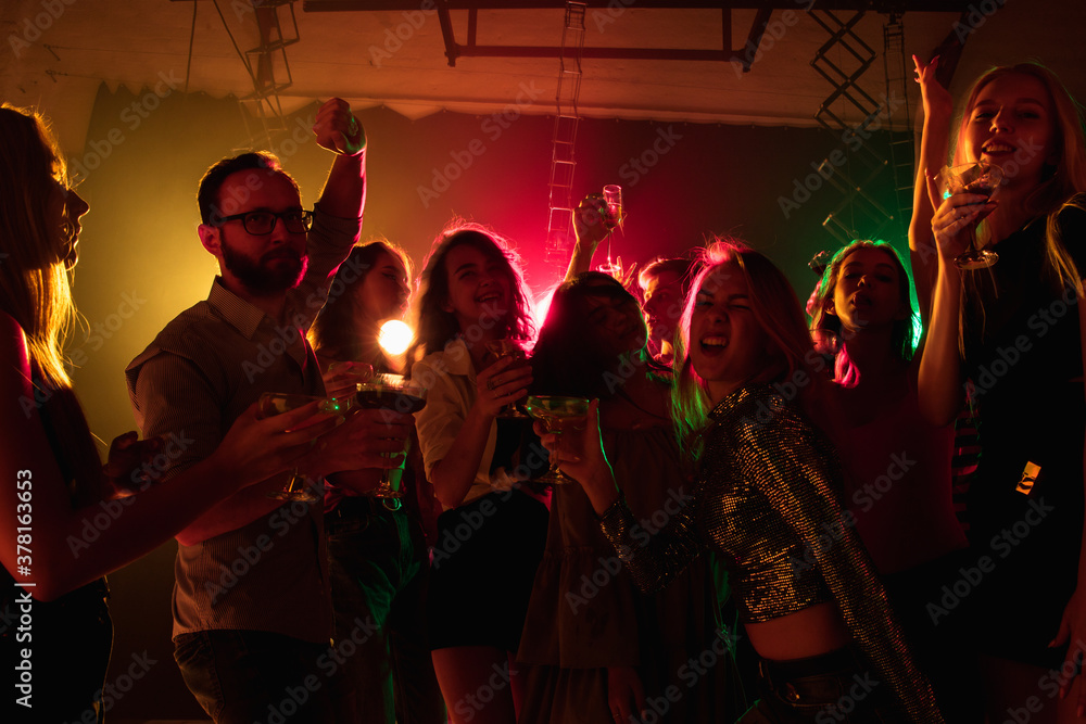Drive. A crowd of people in silhouette raises their hands, dancing on dancefloor on neon light background. Night life, club, music, dance, motion, youth. Bright colors and moving girls and boys.