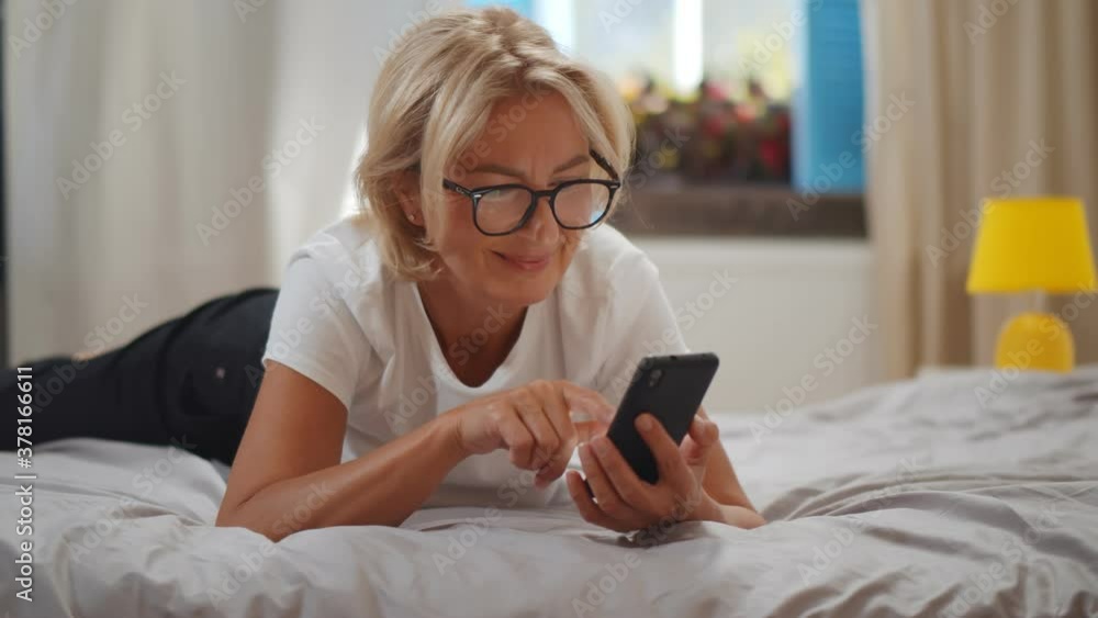 Smiling mature woman lying in bed and checking e-mail on smartphone, Smiling mature woman lying in bed and checking e-mail on smartphone,