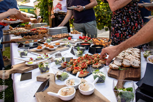 Outdoor garden party with buffet table full of canapes. People serving themselves. Close up of hands taking finger food in their plates.  photo