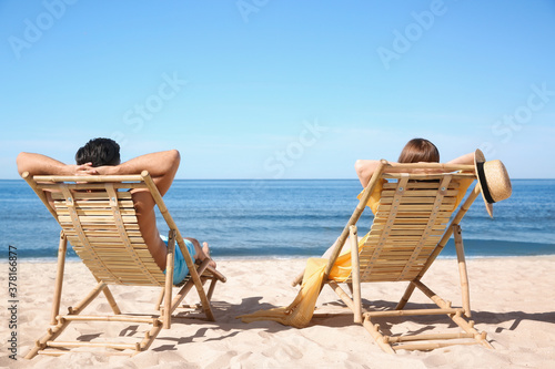 Fototapeta Naklejka Na Ścianę i Meble -  Woman and her boyfriend on deck chairs at beach. Lovely couple