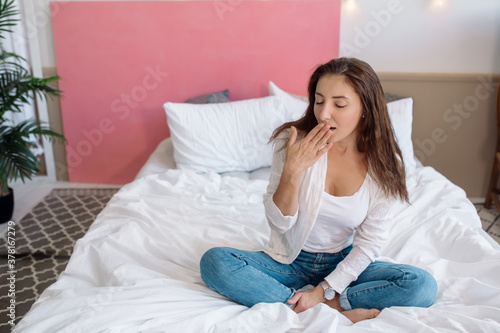 Beautiful sexy slim woman sitting on bed and yawns
