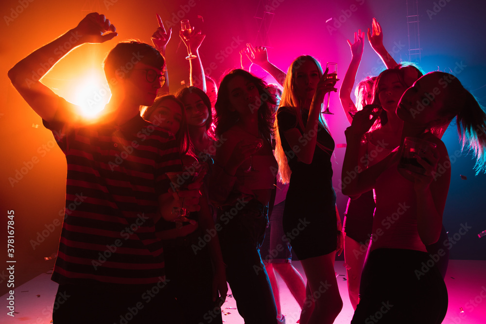 Wild. A crowd of people in silhouette raises their hands, dancing on dancefloor on neon light background. Night life, club, music, dance, motion, youth. Bright colors and moving girls and boys.