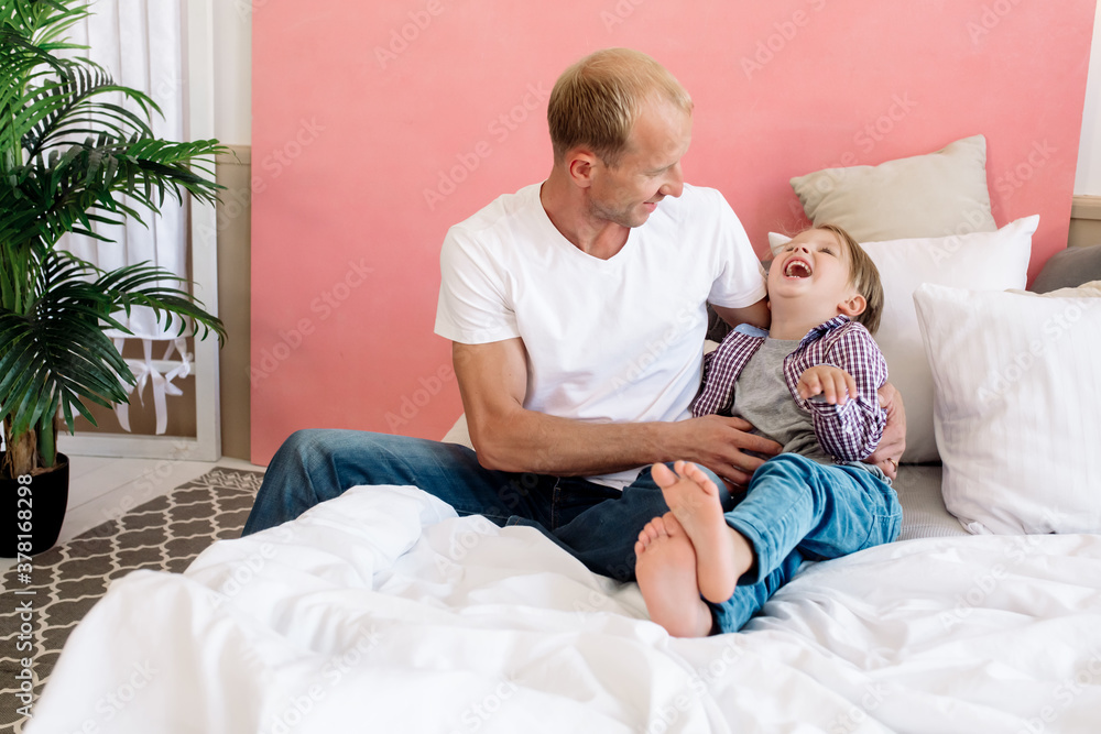 Father and son indulge and play while lying on bed in bedroom at home
