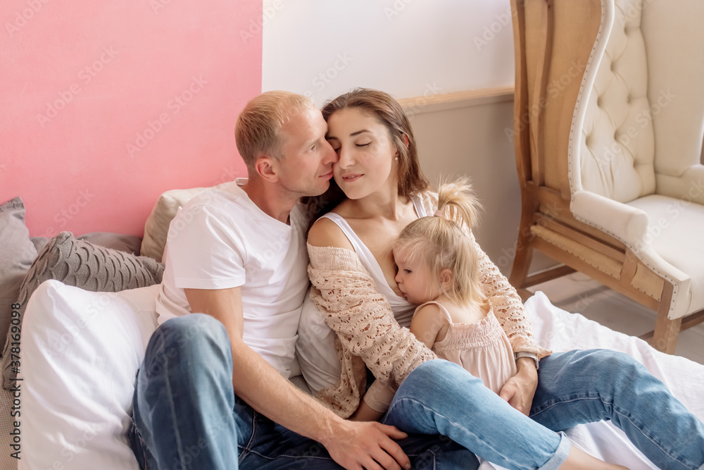 Mom breastfeeds her one-year-old daughter, and father hugs them
Mom breastfeeds her one-year-old daughter, and father hugs them