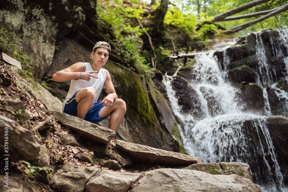 Next to a beautiful waterfall sits a teenage boy and enjoys nature, relaxing in the mountains, gaining strength for the hustle and bustle of the city and college Next to a beautiful waterfall sits a teenage boy and enjoys nature, relaxing in the mountains, gaining strength for the hustle and bustle of the city and college