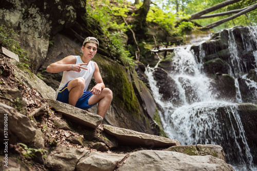 Next to a beautiful waterfall sits a teenage boy and enjoys nature  relaxing in the mountains  gaining strength for the hustle and bustle of the city and college