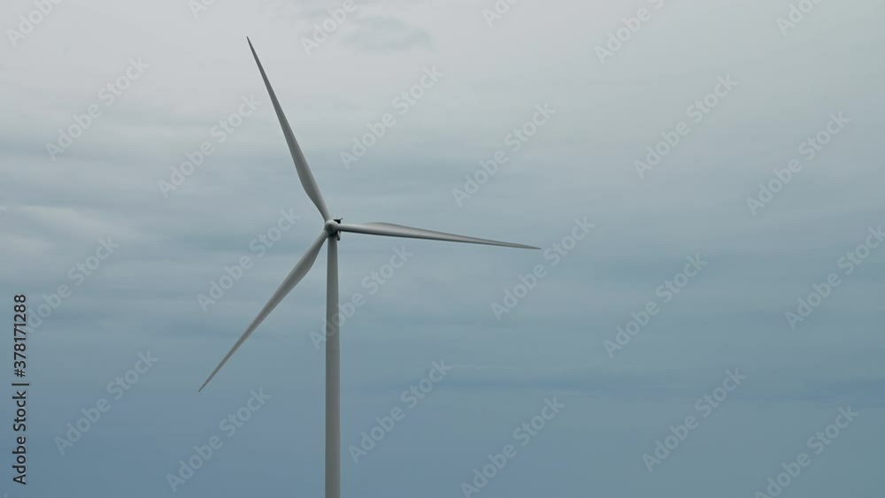 Aerial shot of wind mills rotating by the force of the wind and generating renewable energy in a green ecologic way to the planet on a background of seaside on sunny day. Aerial shot of wind mills rotating by the force of the wind and generating renewable energy in a green ecologic way to the planet on a background of seaside on sunny day.