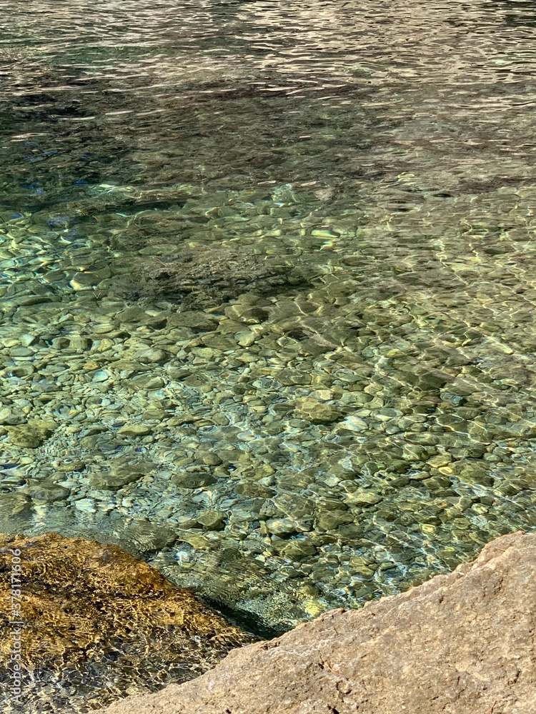 Crystal clear water of Adriatic sea. Pebble seabed. Beautiful sea stones. Refreshing  transparent sea water. Summer in Montenegro. Scenic cobblestones. Clean waters. Relax on the sea shore