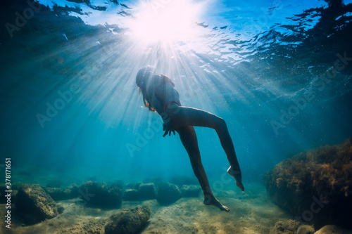 Attractive woman dive near stone with seaweed in underwater. Swimming in transparent sea